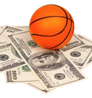 Small basketball ball on heap of dollars isolated on a white background